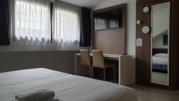 A hotel room with a bed, a desk, a chair, a TV, and a wardrobe.
