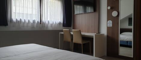 A hotel room with a bed, a desk, a chair, a TV, and a wardrobe.