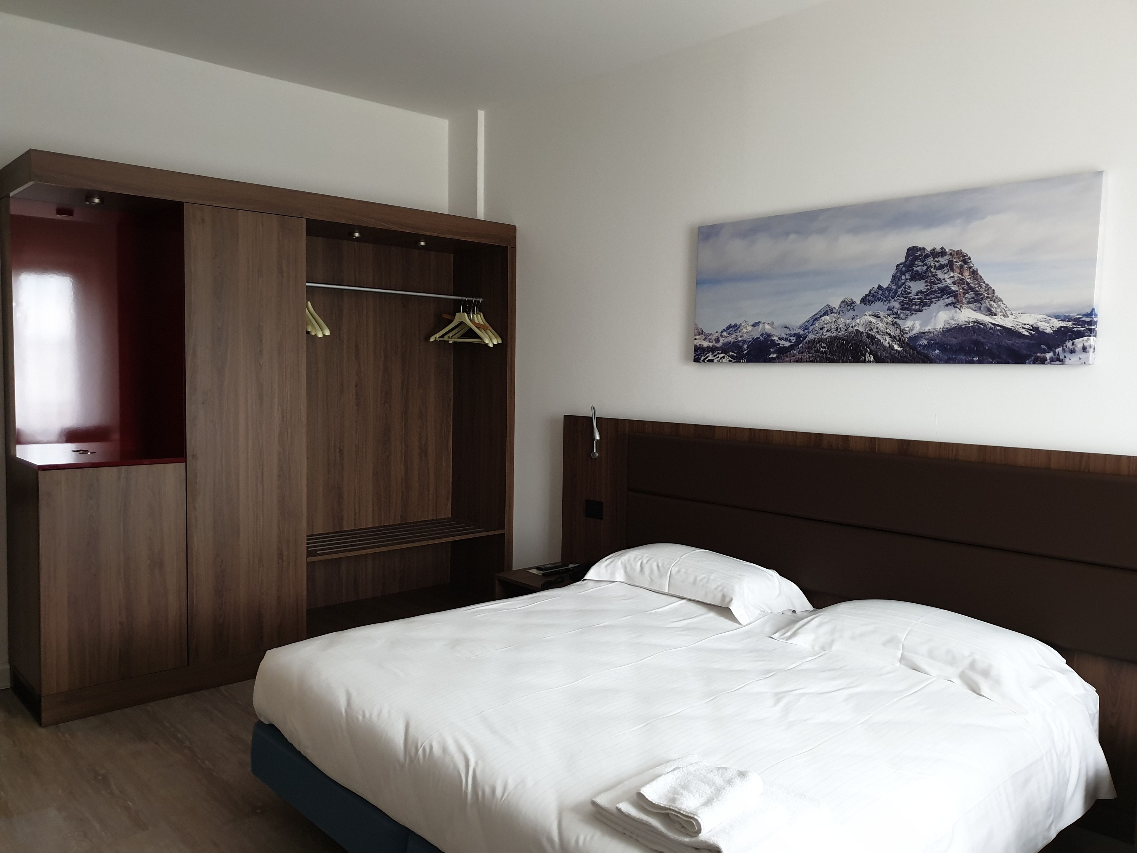 Une chambre d’hôtel avec un lit, une armoire en bois et un tableau représentant un paysage de montagne accroché au mur.