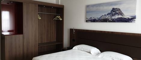 Una habitación de hotel con cama, un armario de madera y una pintura de un paisaje montañoso en la pared.