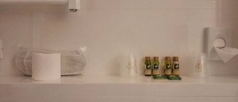 Un baño con un rollo de papel higiénico, una bolsa de plástico y cuatro botellas de loción sobre un mostrador blanco.