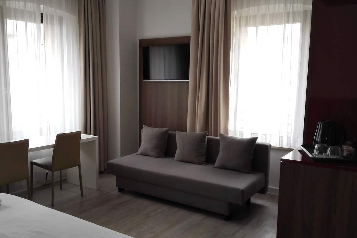 A hotel room with a bed, a desk, a chair, a sofa, and a TV mounted on the wall.