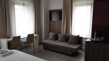 Ein Hotelzimmer mit Bett, Schreibtisch, Sessel, Sofa und einem an der Wand befestigten Fernseher.