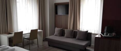A hotel room with a bed, a desk, a chair, a sofa, and a TV mounted on the wall.