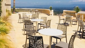 An outdoor patio with round tables and chairs, a view of the landscape, and a palm tree. - Grand Hotel Stella Maris Italia (Palmi)