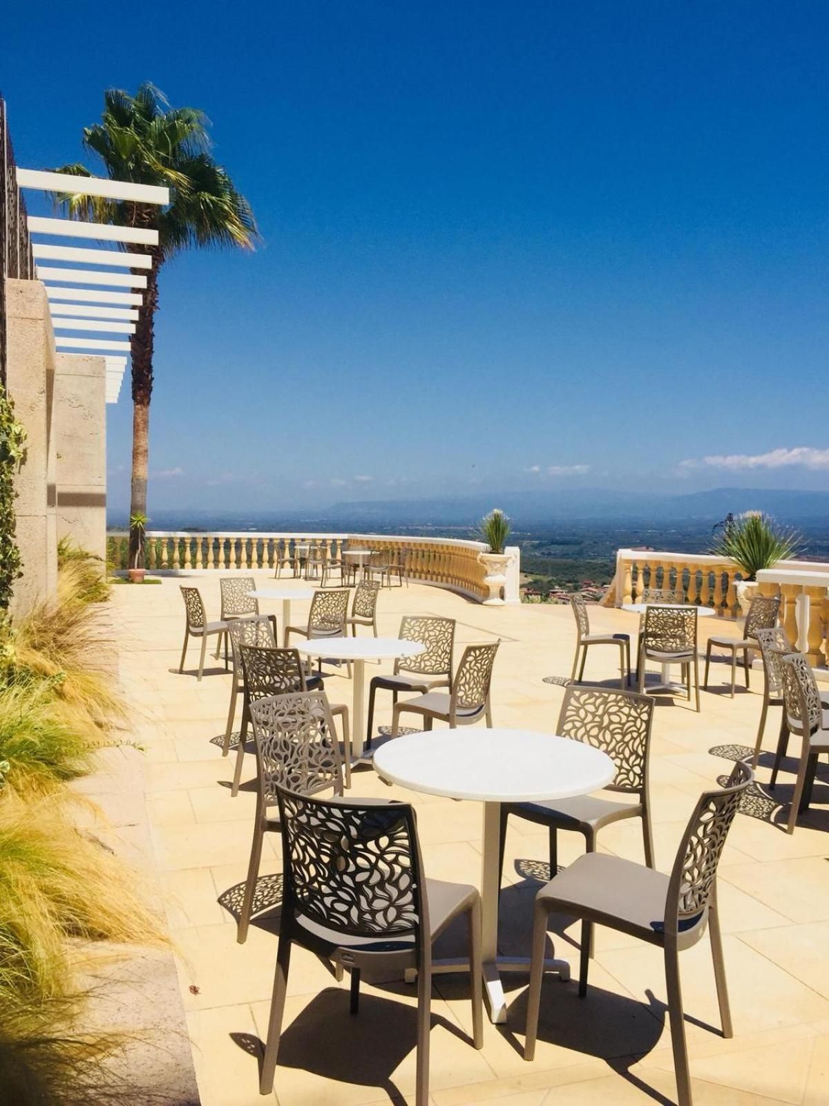 Una terrazza esterna con tavoli e sedie rotonde, vista sul paesaggio e una palma.
