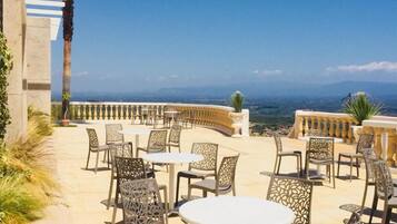 Una terrazza esterna con tavoli e sedie rotonde, vista sul paesaggio e una palma.