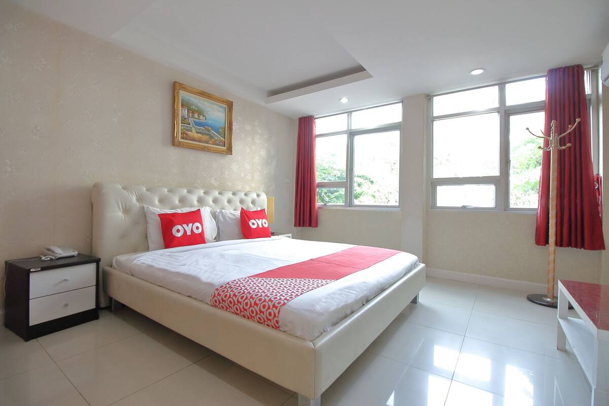 Una habitación de hotel con una cama grande, una mesita de noche, un cuadro en la pared y una ventana con cortinas.