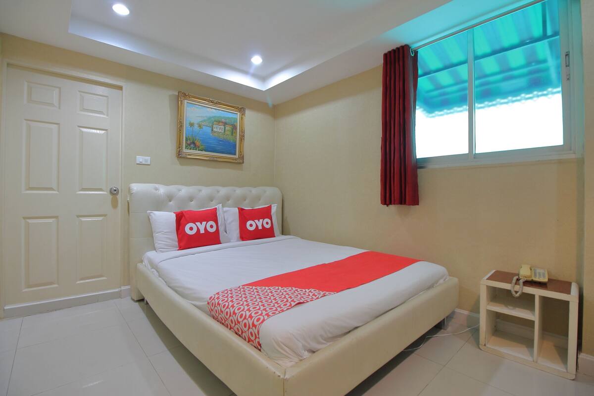 Un dormitorio con cama, un cuadro en la pared, una ventana con cortinas y una mesita de noche con teléfono.