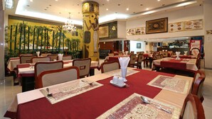En restaurang med bord uppställda för servering, med en central, dekorativ pelare prydd med hieroglyfer, inramade konstverk på väggarna och en bardisk i bakgrunden.