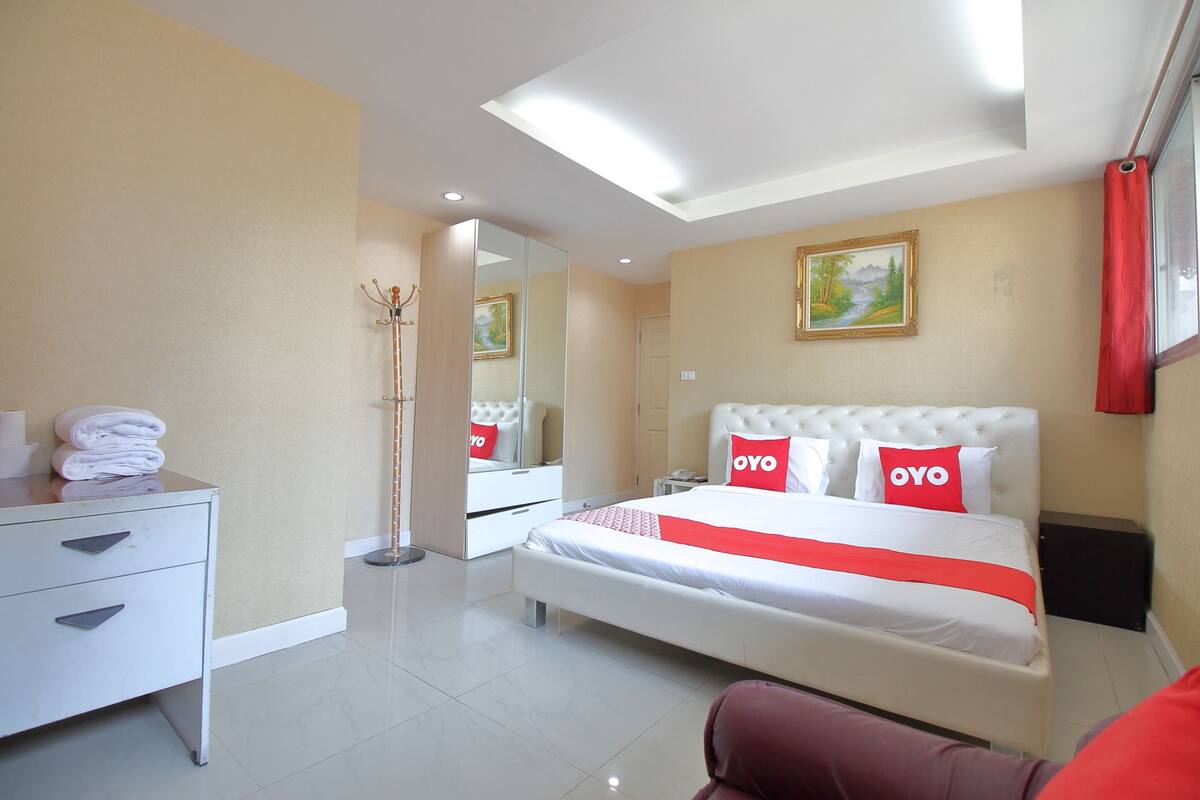 Habitación de hotel moderna con una cama bien hecha, un tocador blanco, un espejo y un cuadro en la pared.