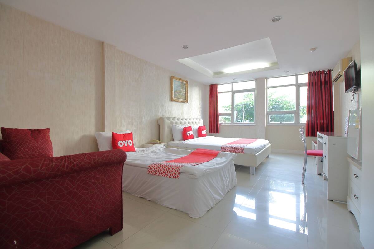 Habitación de hotel con dos camas, un sofá, un televisor y una ventana con cortinas rojas.