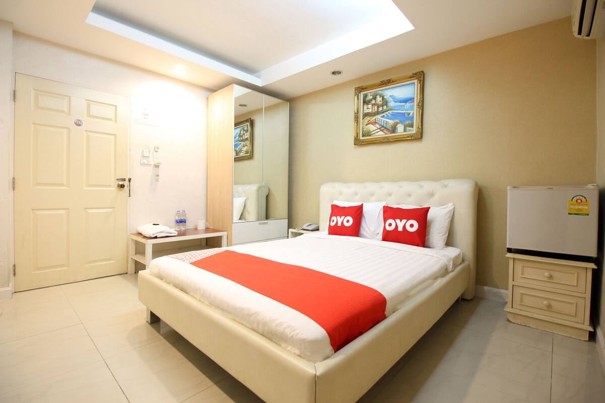 Habitación de hotel con una cama grande, una mesita de noche, un espejo, un refrigerador y una puerta.