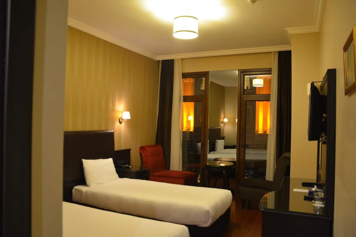 A hotel room with two beds, a desk, a chair, and a TV.