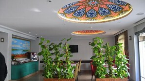 Un vestíbulo de hotel con un gran diseño de techo ornamentado, una pintura en la pared y plantas en macetas al frente.