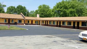 A motel with multiple rooms, a parking lot, and a grassy area with a child. - Royal Inn (Tonawanda)