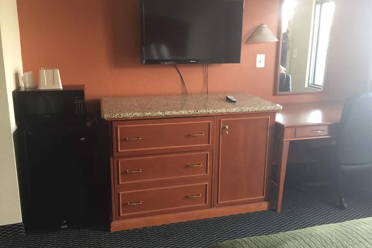A hotel room with a wooden cabinet, a microwave, a flat-screen TV, and a desk with a chair.