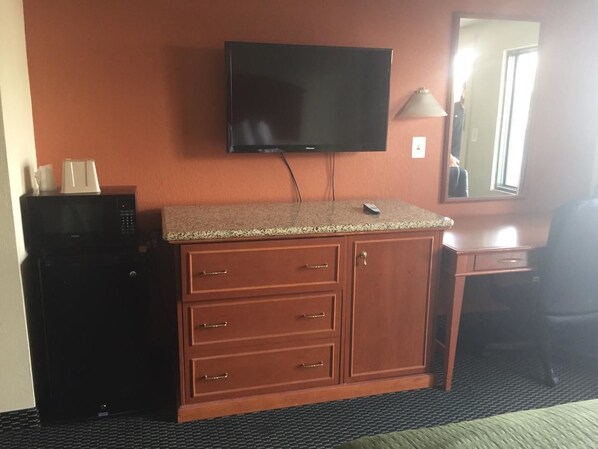 Habitación de hotel con un armario de madera, microondas, televisor de pantalla plana y escritorio con silla.