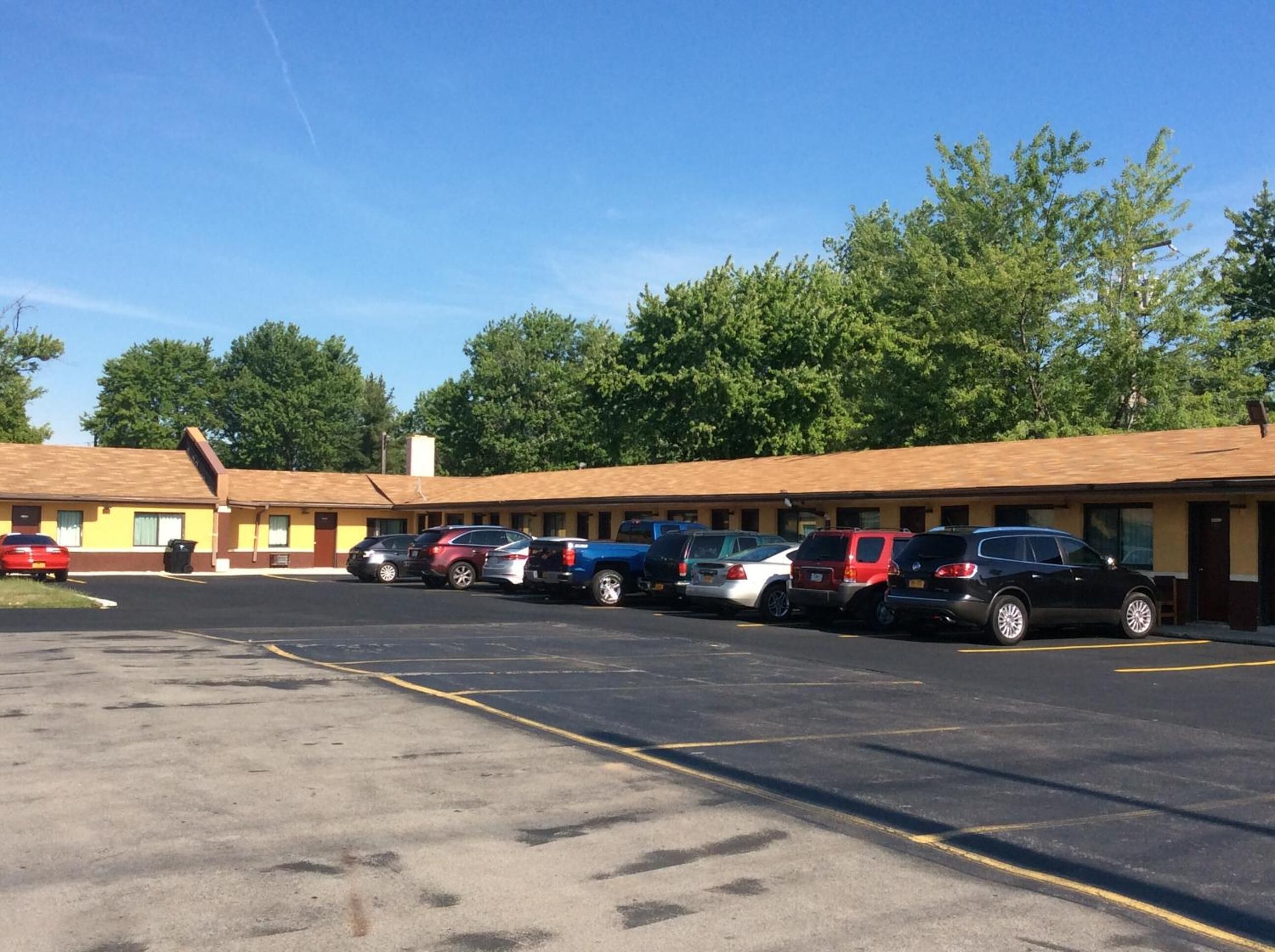 A motel with a row of parking spaces and a building with a yellow facade and brown roof.