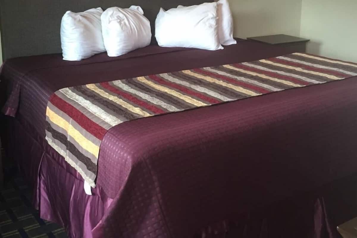 A hotel room with a large bed, a headboard, a striped blanket, and a dark headboard.