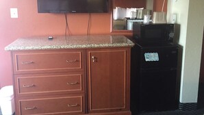 A kitchenette with a granite countertop, a microwave, and a television mounted above the counter. - Royal Inn (Tonawanda)