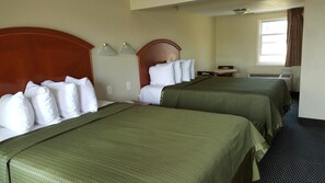 Habitación de hotel con dos camas, cada una con ropa de cama verde y almohadas blancas, un cabecero de madera, una mesita pequeña y una ventana con cortinas.