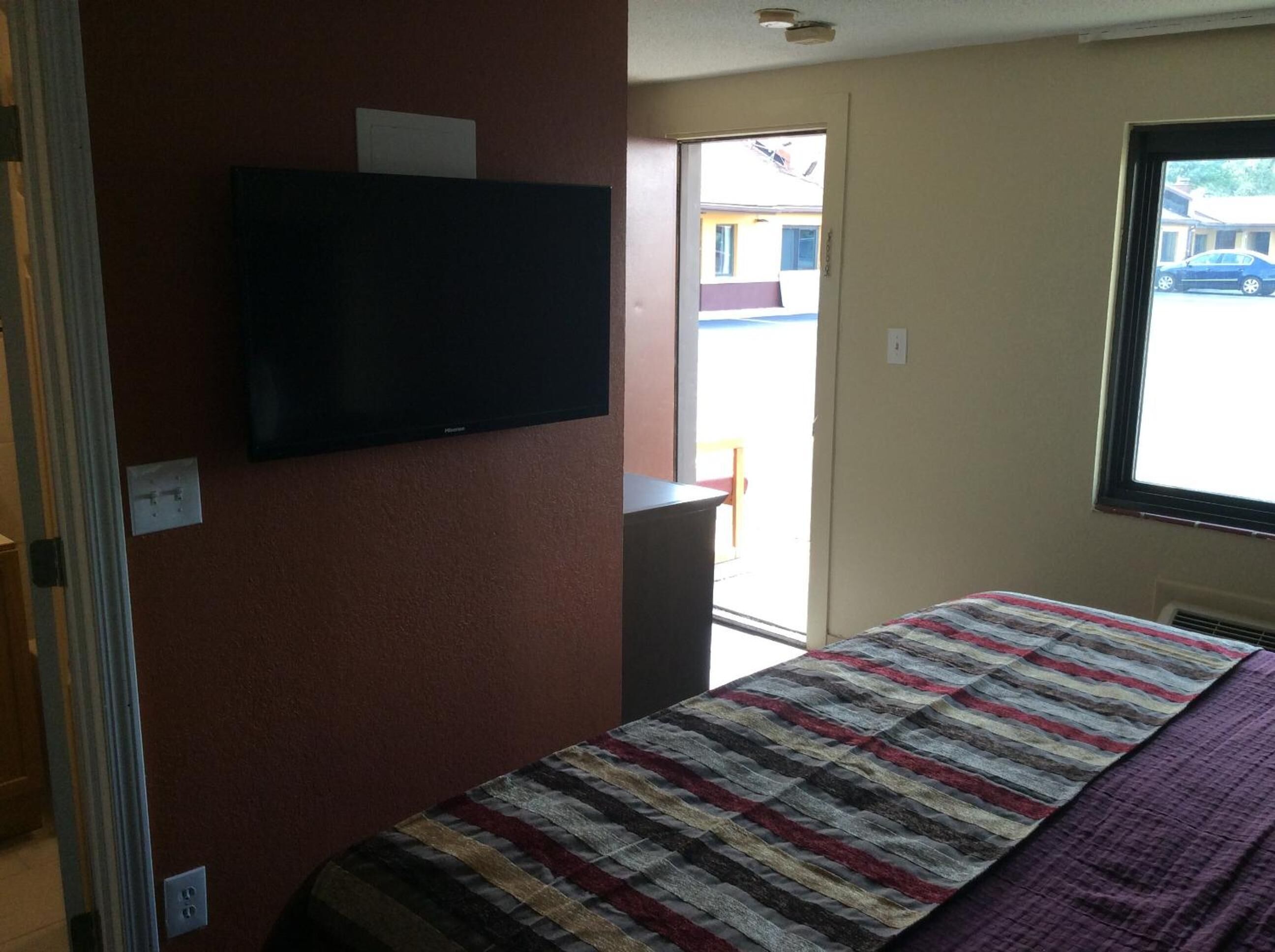 A room with a bed, a television mounted on the wall, and a window with a view of the outside.