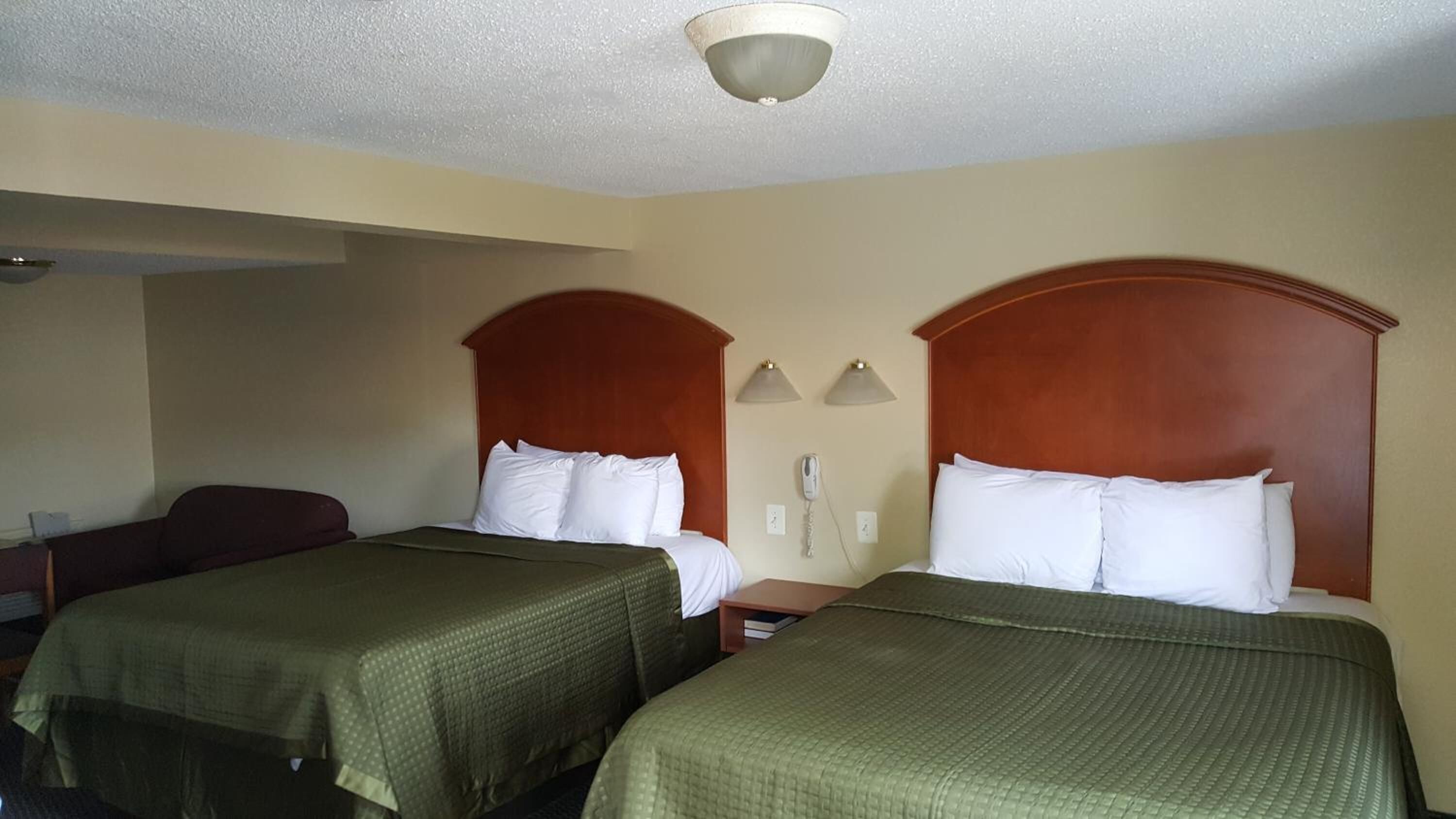 A hotel room with two beds, each with a wooden headboard and white bedding. There are two bedside tables with lamps and a phone on one wall.