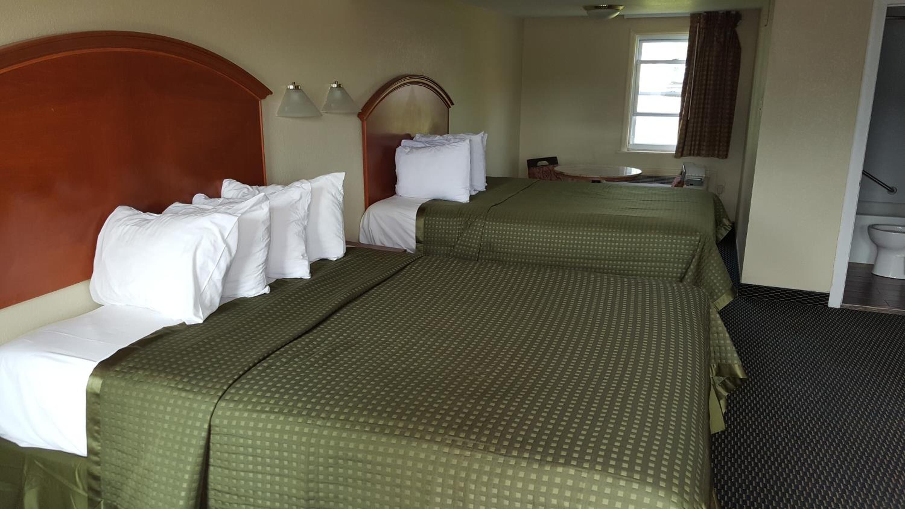 A hotel room with two beds, a small table, a mirror, and a window.