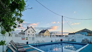 A rectangular swimming pool with lounge chairs and a white fence.