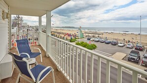A balcony with blue chairs, a view of a beach, and a parking area with cars.