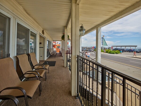 A covered porch with seating, a view of the street, and a gas station in the background. - The Hillcrest (Hampton)