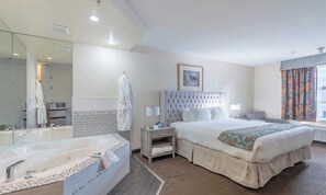 Une chambre d’hôtel avec un grand lit, une salle de bain séparée avec une baignoire, une table de chevet avec une lampe et une fenêtre avec des rideaux.