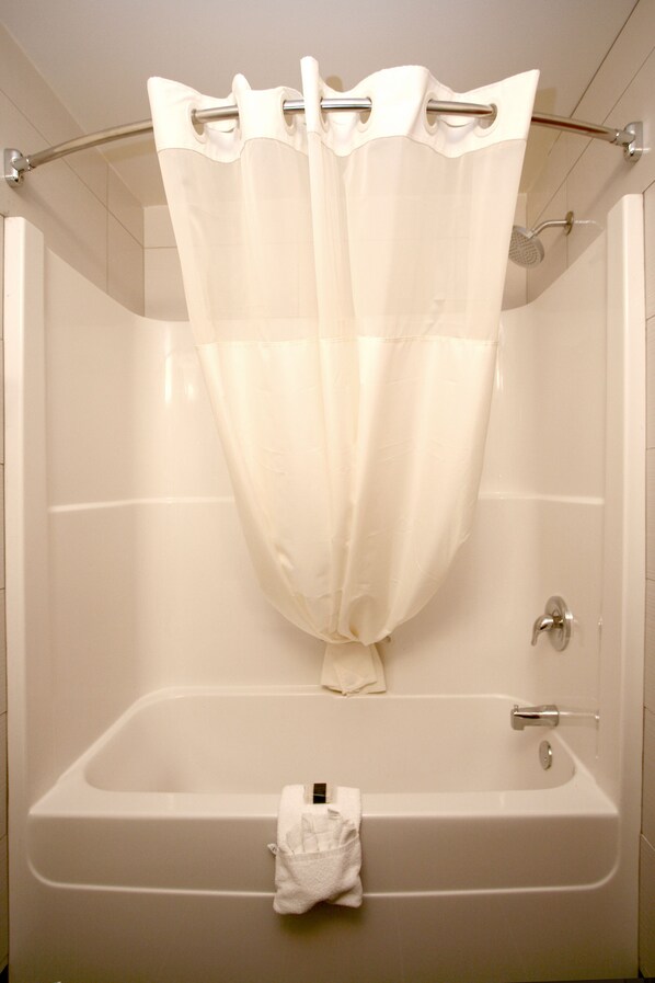 Une baignoire blanche avec un rideau de douche, une serviette et un pommeau de douche à main.