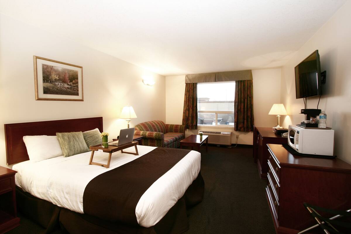 A hotel room with a large bed, a sofa, a desk with a computer, a TV, and a window with curtains.
