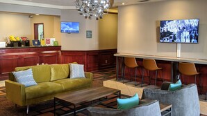 A hotel lobby with a reception desk, a yellow sofa, a coffee table, and a bar area with chairs. - Foxwood Inn & Suites (Drayton Valley)