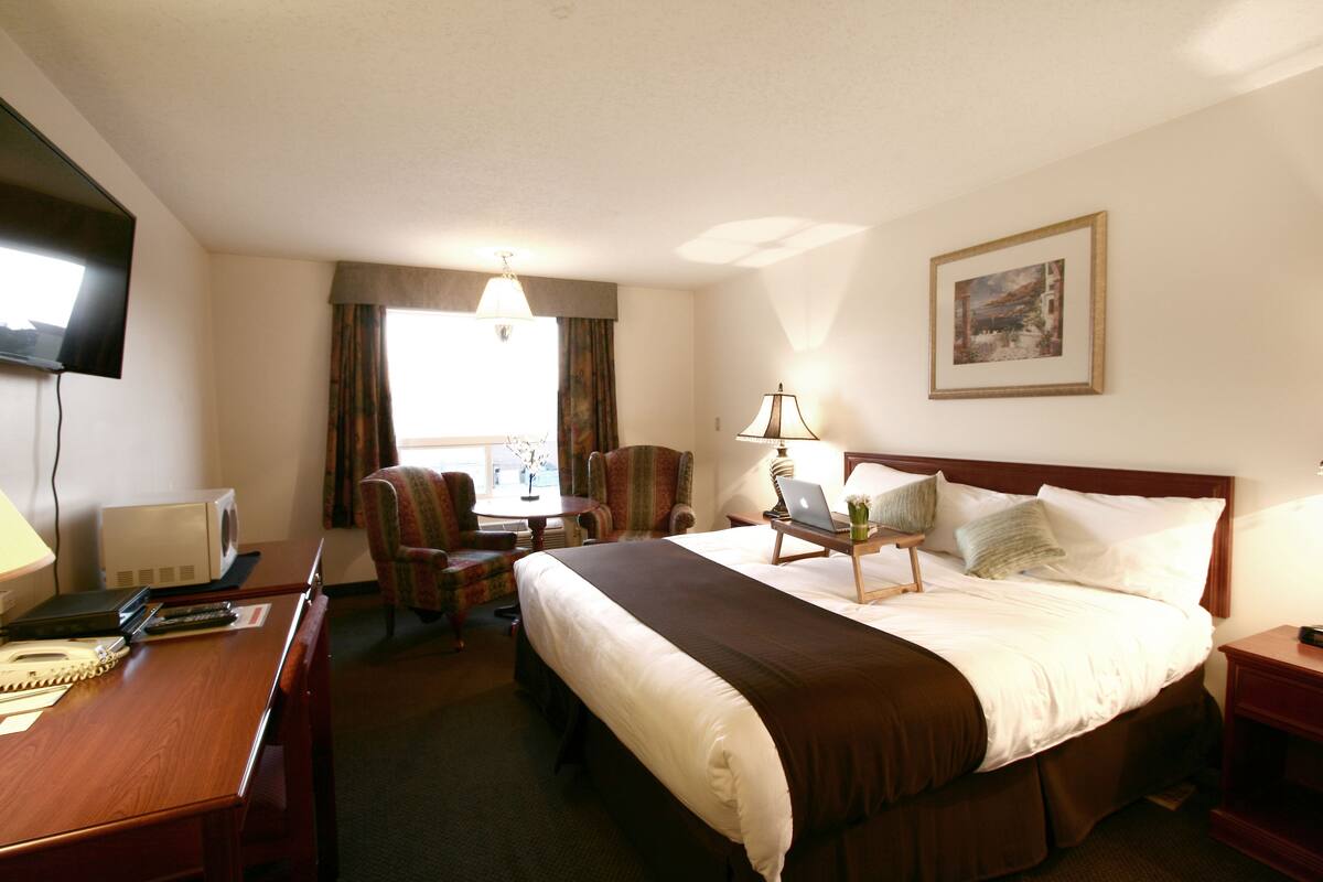 A hotel room with a bed, desk, chair, lamp, and a painting on the wall.