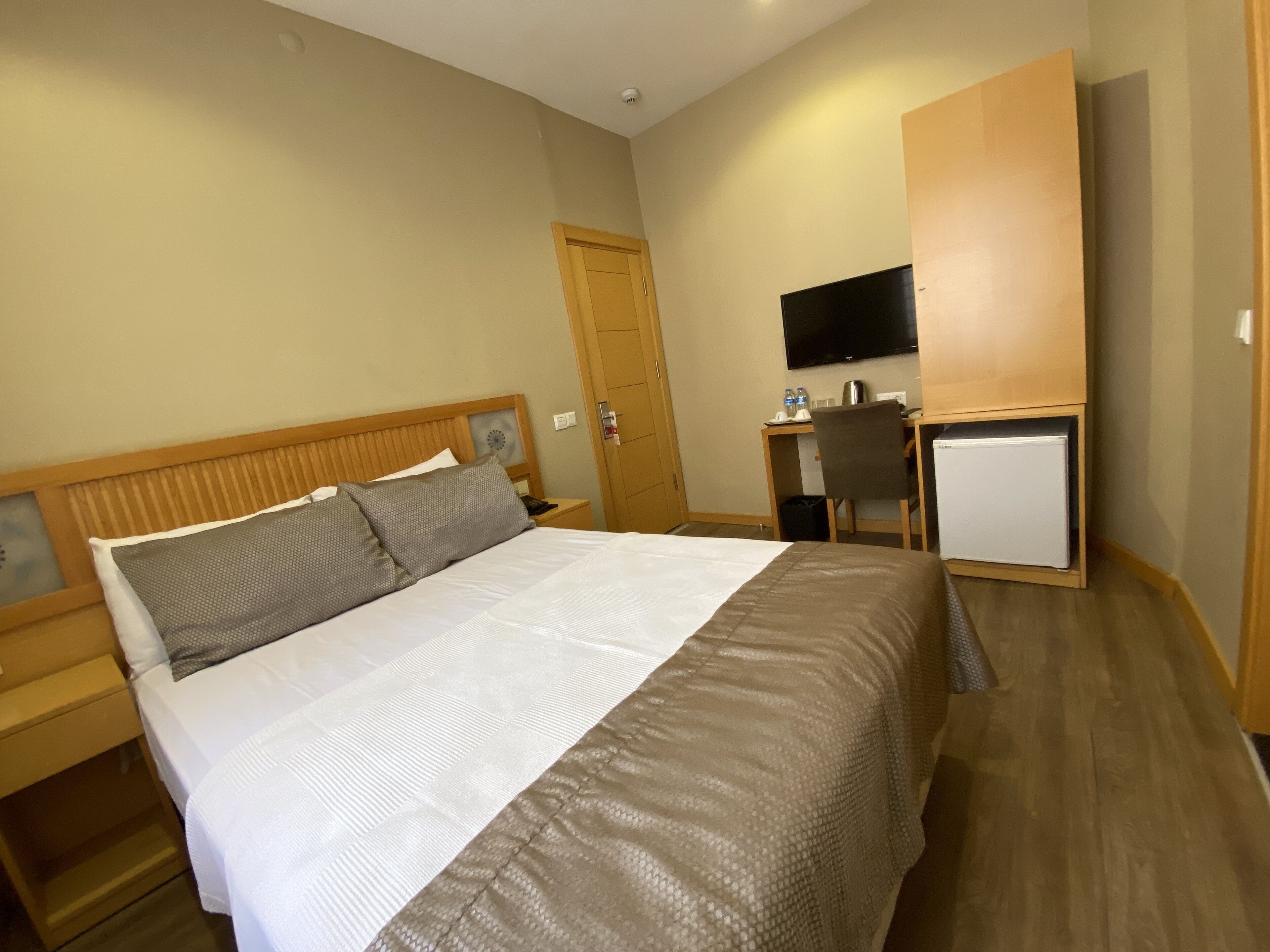 A hotel room with a large bed, a desk with a chair, a television, and a wardrobe.