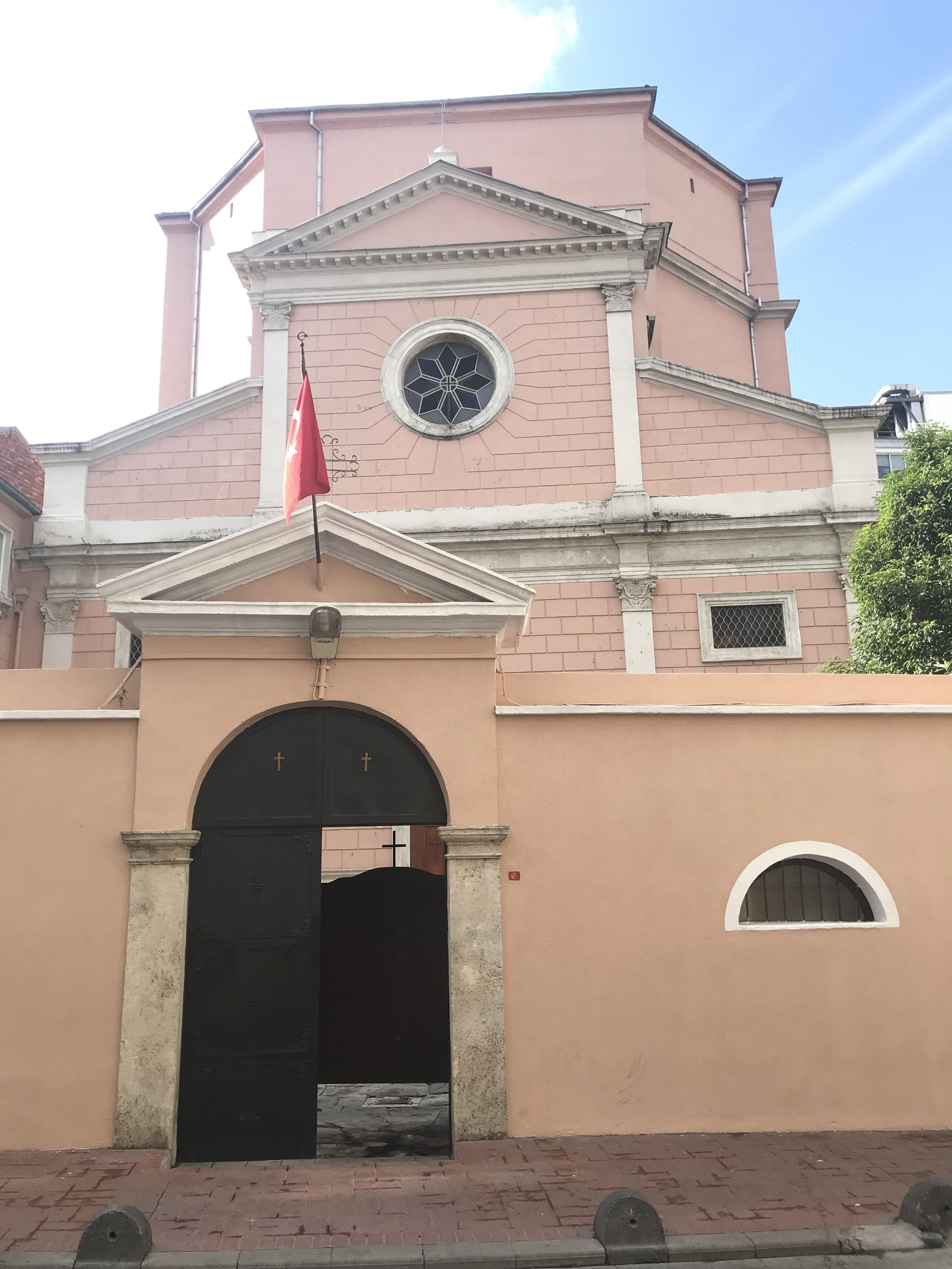 A building with a pink facade, a black entrance gate, and a flag.