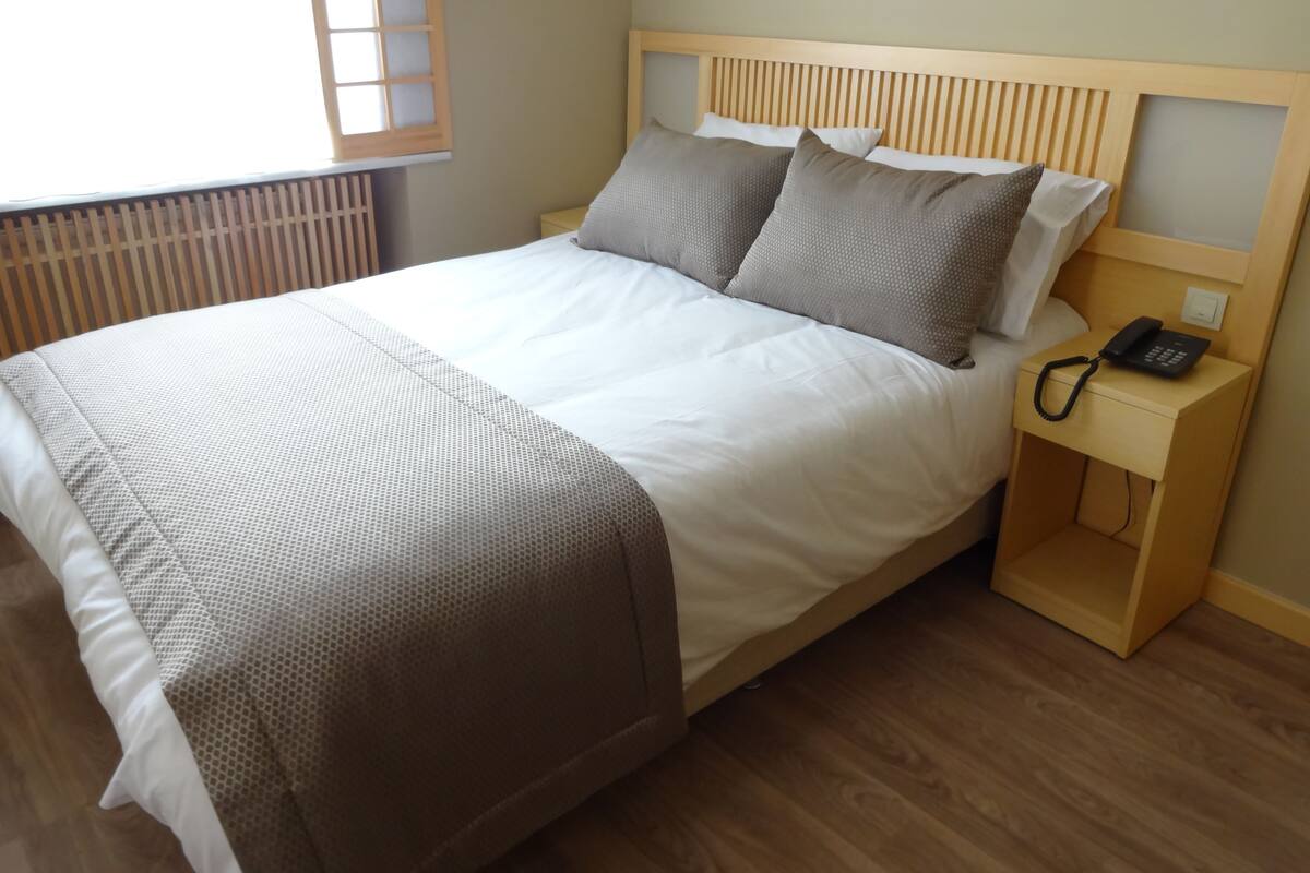 A neatly made bed with a wooden headboard, a bedside phone, and a small wooden nightstand.