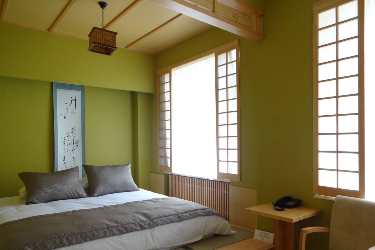A neatly made bed with pillows, a small bedside table with a phone, and a chair.