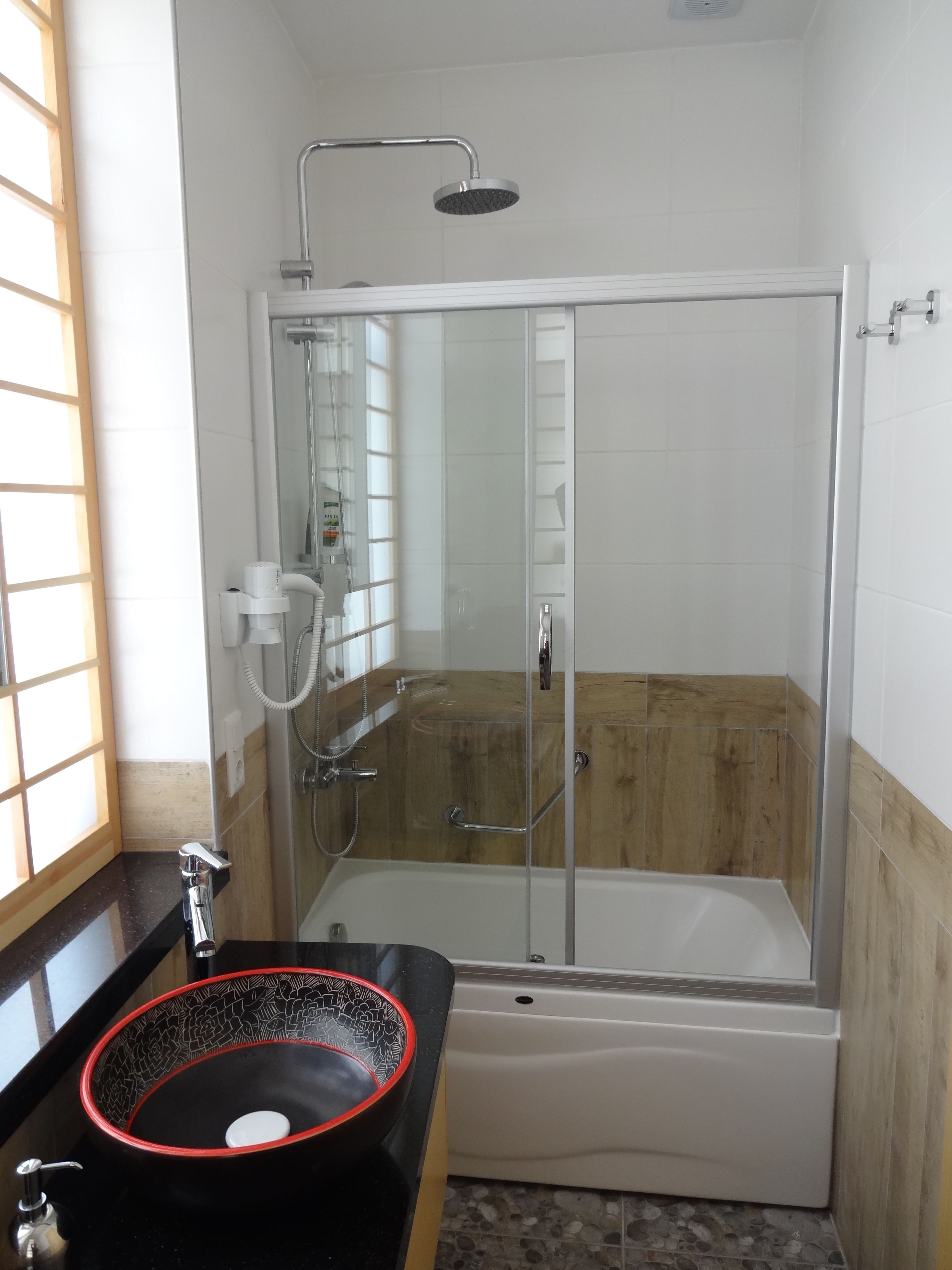 Une salle de bain moderne avec une douche en verre, un lavabo noir avec un bord rouge et une baignoire.