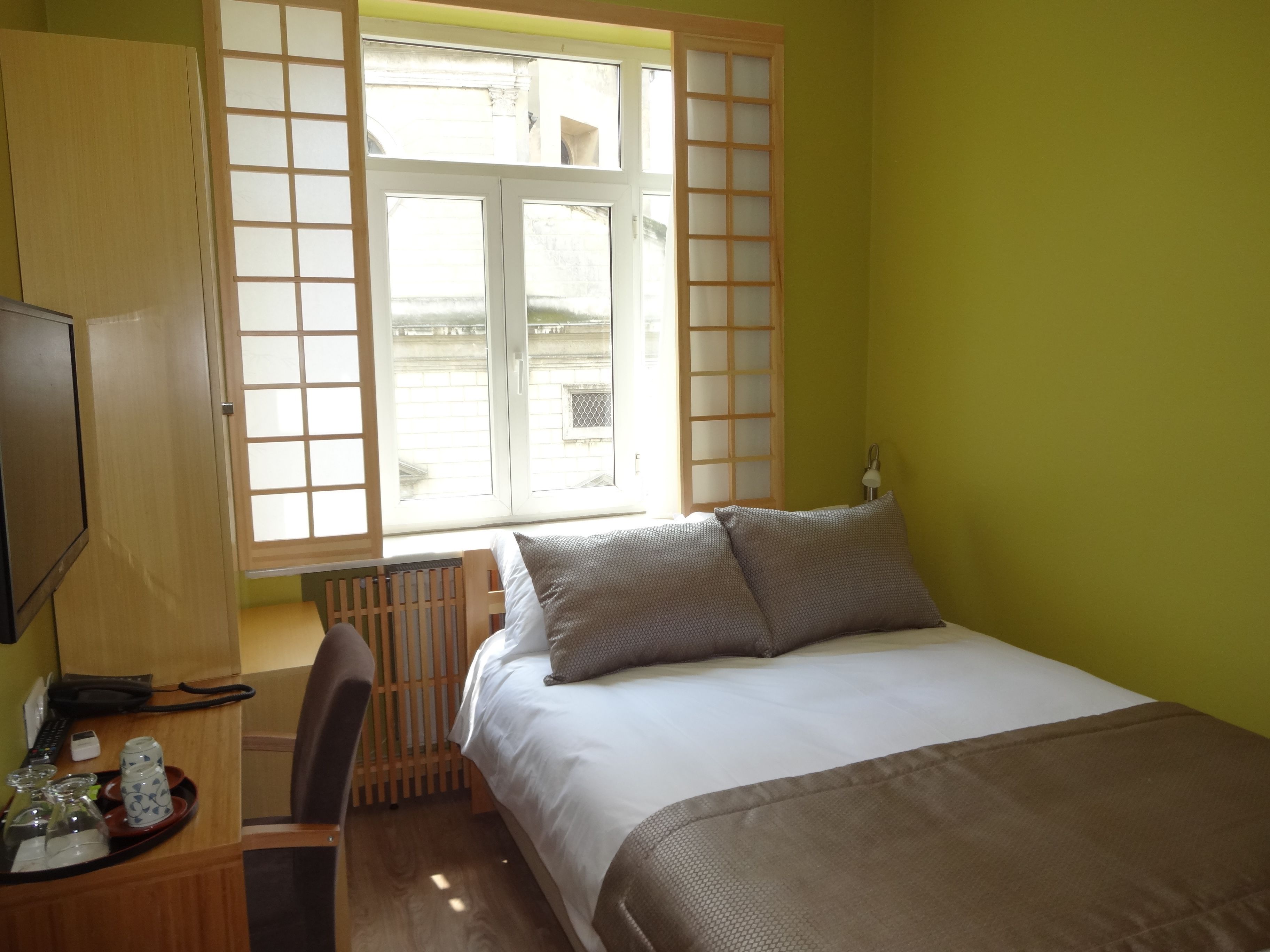 Une chambre d’hôtel comprenant un lit, un bureau avec une chaise, une télévision et une fenêtre donnant sur l’extérieur.
