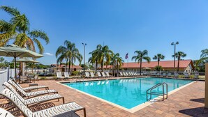 A pool area with lounge chairs, palm trees, and a clear blue sky.