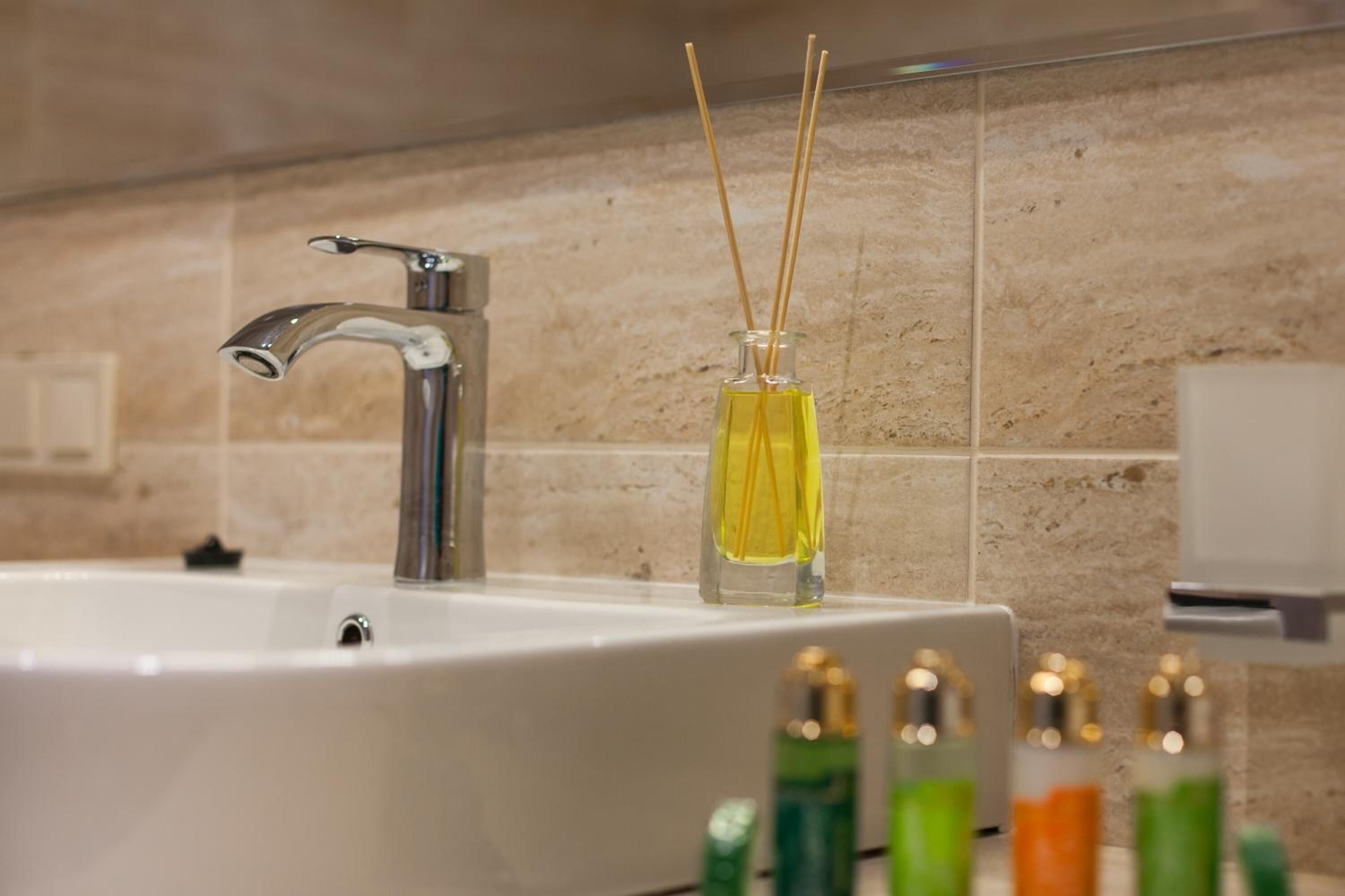 A bathroom sink with a modern faucet and a glass bottle with reed sticks.