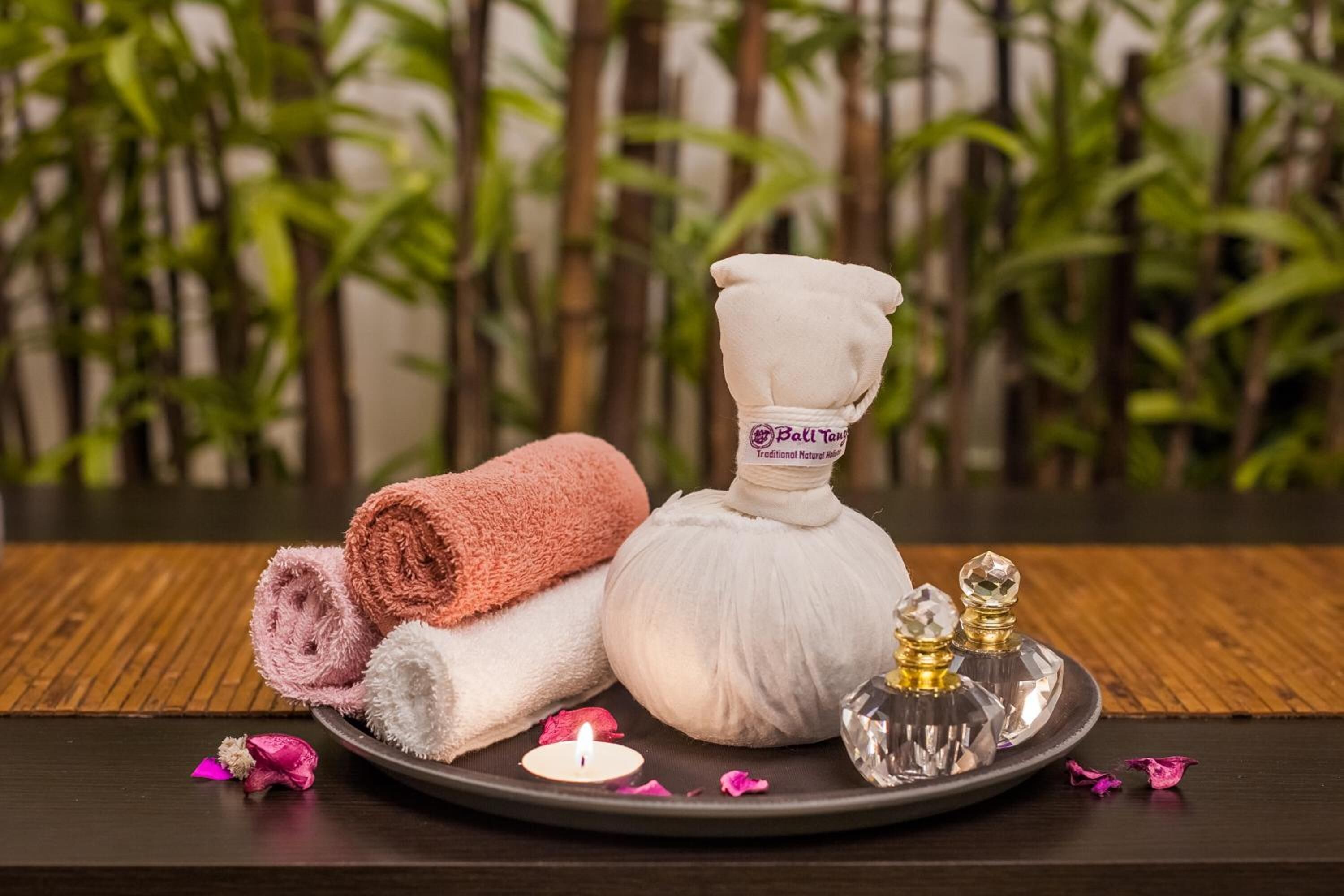 A spa setting with towels, a massage oil bottle, and a candle on a tray.