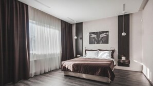 Une chambre moderne avec un grand lit, un parquet en bois foncé, des rideaux légers et un luminaire fixé au mur.