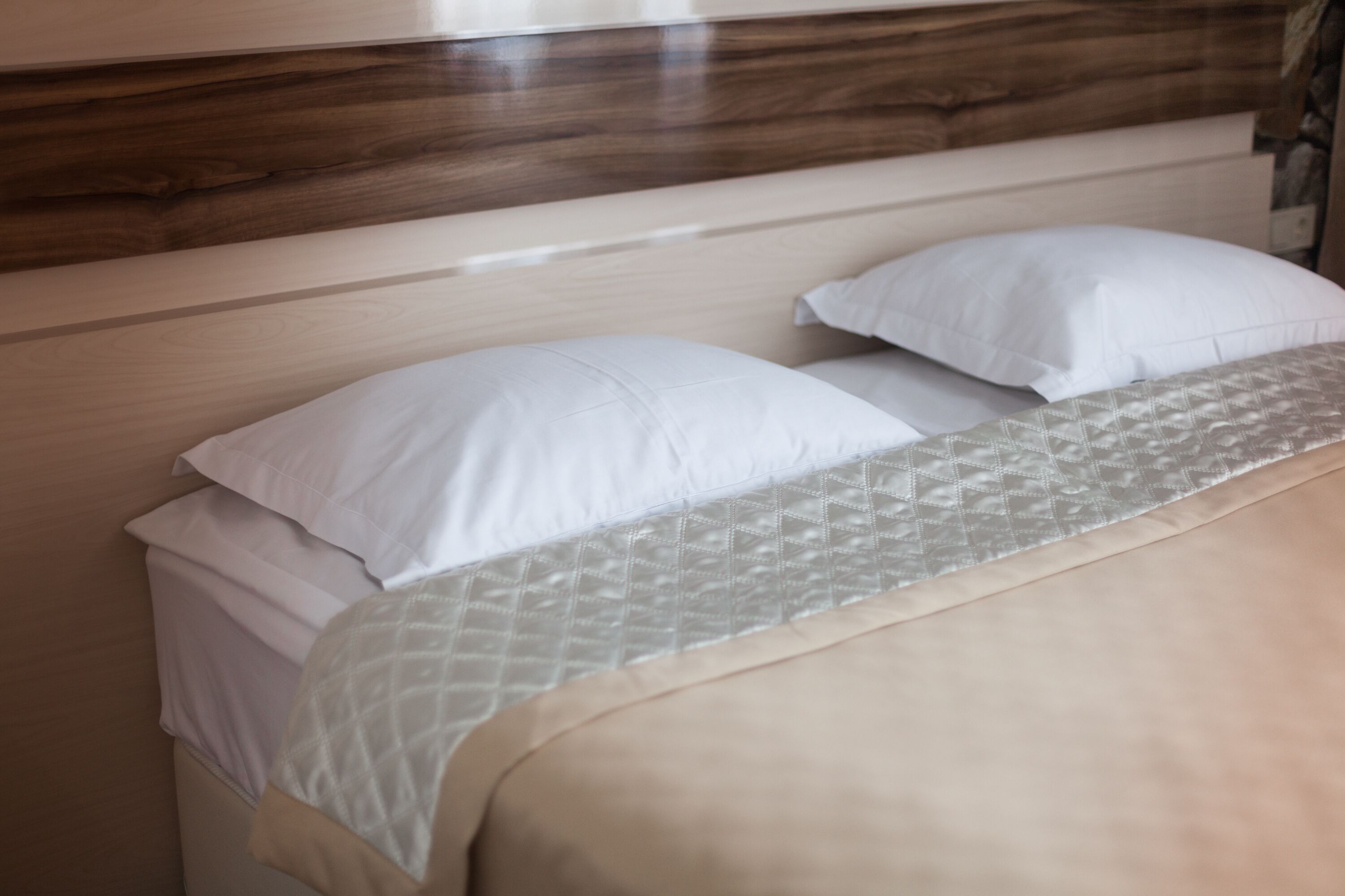 Ein Bett mit Holz-Kopfteil, weißen Kissen und einer gemusterten Tagesdecke.