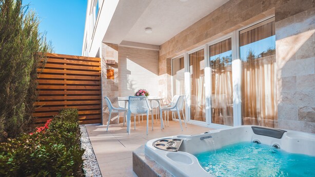 Une terrasse extérieure moderne, dotée d’un jacuzzi, de chaises blanches et d’une clôture en bois.