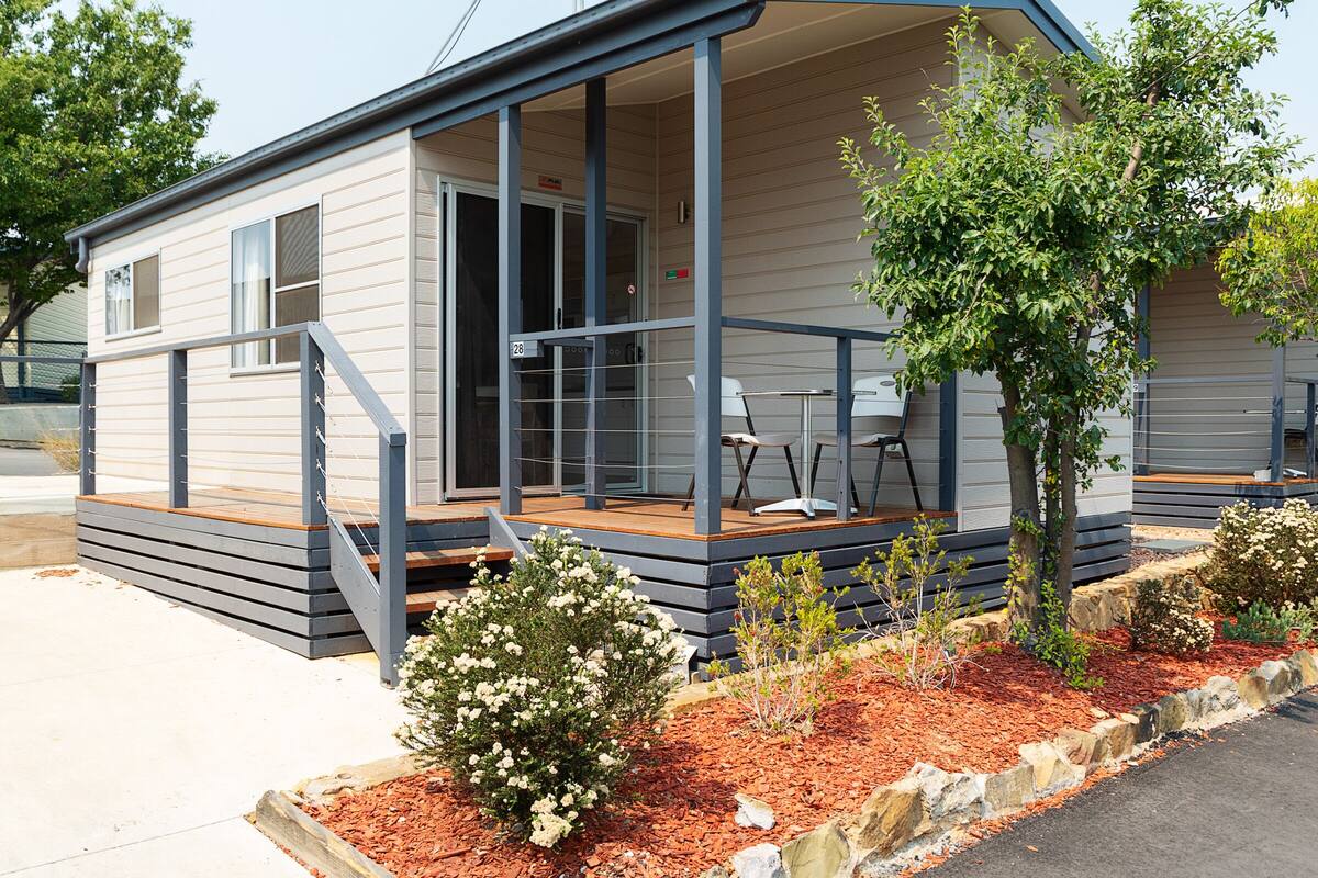 A small, single-story mobile home with a porch, outdoor seating, and a small garden area.